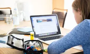 Dziewczynka uczy się przy laptopie, co pokazuje, czy nauczanie indywidualne może być prowadzone zdalnie. Na biurku przybory szkolne i butelka wody.