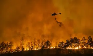 Helikopter zrzuca wodę na płonący las. Intensywny pomarańczowy dym i ogień to przerażające skutki globalnego ocieplenia.