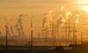 Dymiące kominy fabryk i linie energetyczne na tle zachodzącego słońca symbolizują antropogeniczne zmiany klimatu.