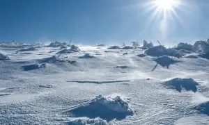Mroźny krajobraz Antarktydy zimą. Słońce przebija się przez chmury, a wiatr rzeźbi śnieg. Pytanie, ile stopni jest na Antarktydzie zimą, pozostaje bez odpowiedzi.