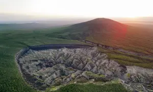 Krajobraz Syberii z gigantycznym kraterem, który powstał w wyniku topnienia wiecznej zmarzliny inaczej. Wokół lasy i wzgórza.