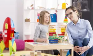 Nauczycielka z tablicą, na której dziecko liczy. Czy zajęcia wyrównawcze są obowiązkowe? Dziecko uczy się liczyć na liczydle.
