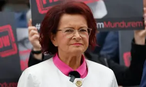 Kobieta w okularach i białej marynarce, z czerwonymi włosami, na tle transparentów. To może być klimatyczna bzdura roku.