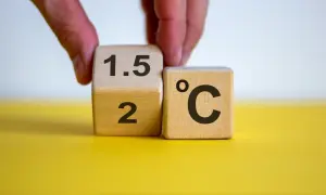 Dłoń obraca kostkę z "2" na "1.5", symbolizując cel paryskiego porozumienia klimatycznego.