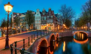 Most Amsterdam canals are a punkt wyjściowy do pomiarów wysokości na lądzie. Widok na kanał z mostem oświetlonym lampkami i kamienicami w tle.