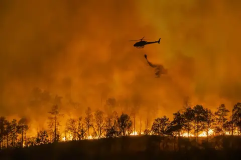 Helikopter zrzuca wodę na płonący las. Intensywny pomarańczowy dym i ogień to przerażające skutki globalnego ocieplenia.