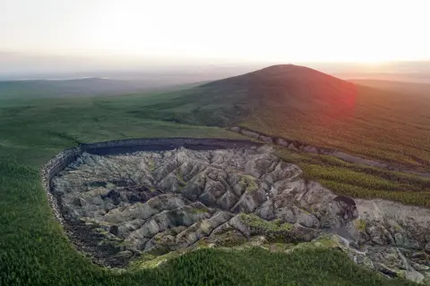 Krajobraz Syberii z gigantycznym kraterem, który powstał w wyniku topnienia wiecznej zmarzliny inaczej. Wokół lasy i wzgórza.