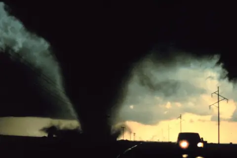 Potężny lejek tornado zbliża się do drogi, gdzie jedzie samochód. To przerażające skutki cyklonów tropikalnych.