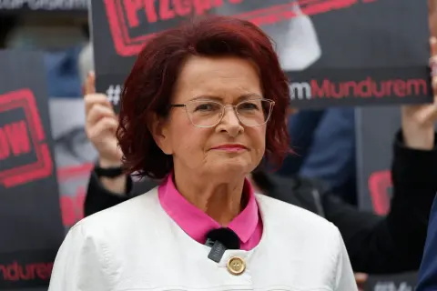 Kobieta w okularach i białej marynarce, z czerwonymi włosami, na tle transparentów. To może być klimatyczna bzdura roku.