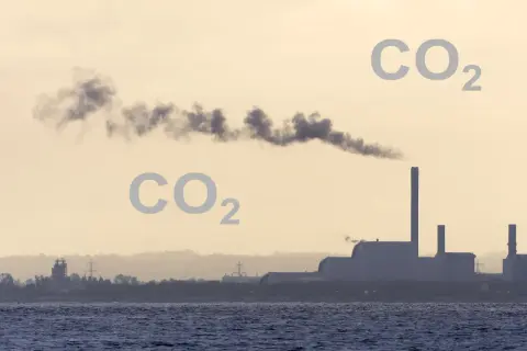 Dym z fabryki unosi się w powietrzu, a obok pojawia się napis CO2, sugerując, czy dwutlenek węgla jest cięższy od powietrza.