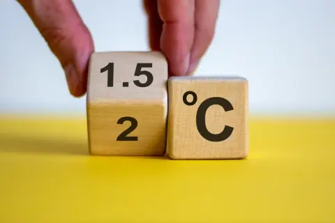 Dłoń obraca kostkę z "2" na "1.5", symbolizując cel paryskiego porozumienia klimatycznego.