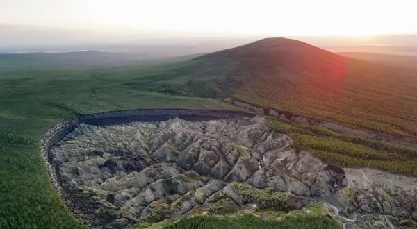 Krajobraz Syberii z gigantycznym kraterem, który powstał w wyniku topnienia wiecznej zmarzliny inaczej. Wokół lasy i wzgórza.