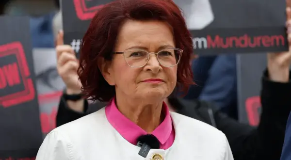 Kobieta w okularach i białej marynarce, z czerwonymi włosami, na tle transparentów. To może być klimatyczna bzdura roku.