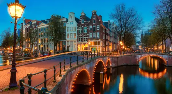 Most Amsterdam canals are a punkt wyjściowy do pomiarów wysokości na lądzie. Widok na kanał z mostem oświetlonym lampkami i kamienicami w tle.