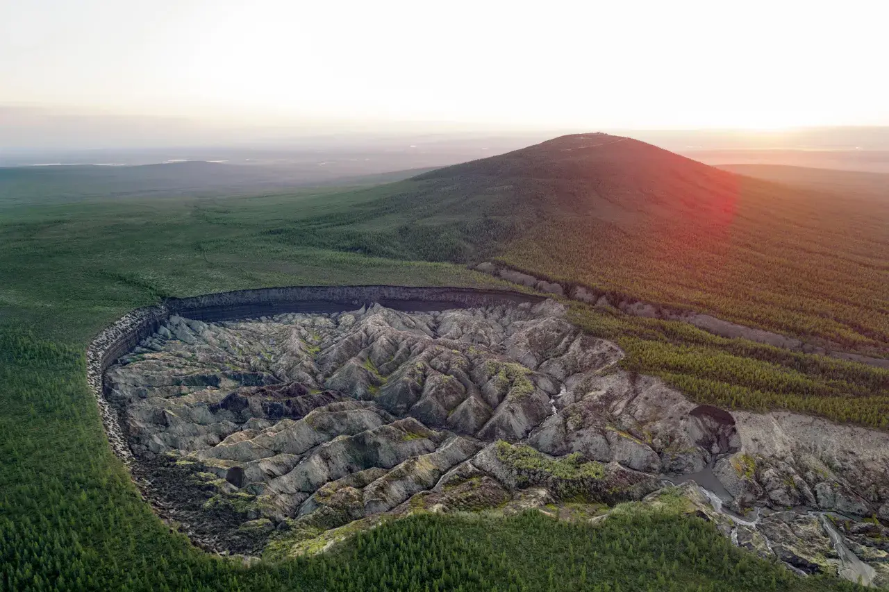 Krajobraz Syberii z gigantycznym kraterem, który powstał w wyniku topnienia wiecznej zmarzliny inaczej. Wokół lasy i wzgórza.