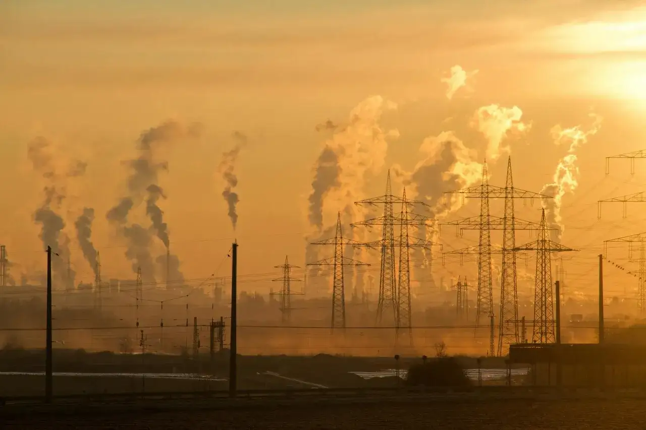 Dymiące kominy fabryk i linie energetyczne na tle zachodzącego słońca symbolizują problemy związane ze zmianami klimatycznymi na Ziemi.