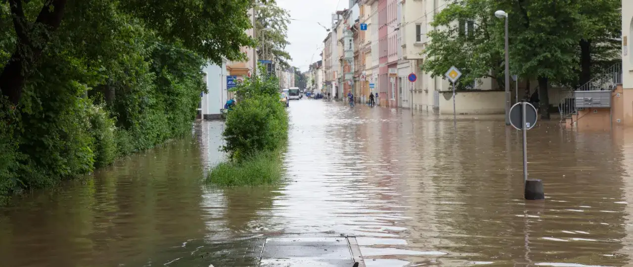 Zalana ulica w mieście, ludzie brodzą w wodzie. To smutny obraz skutków antropogenicznych zmian klimatu.