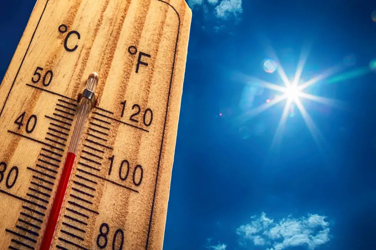 Drewniany termometr pokazuje wysoką temperaturę, a słońce świeci na błękitnym niebie.
