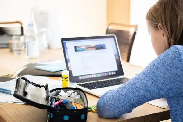 Dziewczynka uczy się przy laptopie, co pokazuje, czy nauczanie indywidualne może być prowadzone zdalnie. Na biurku przybory szkolne i butelka wody.