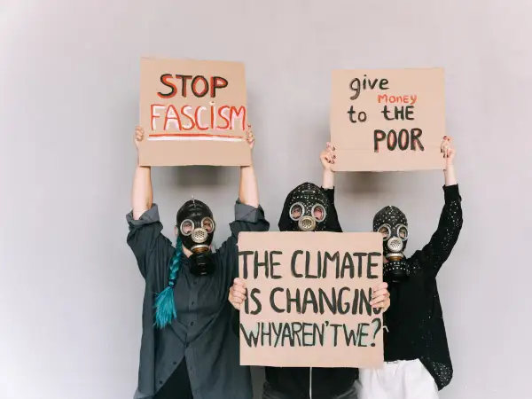 Trzy osoby w maskach gazowych trzymają transparenty: "STOP FASZYZM", "Daj pieniądze biednym" i "Klimat się zmienia, a my?". Ziemia na rozdrożu.