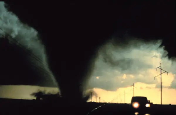 Potężny lejek tornado zbliża się do drogi, gdzie jedzie samochód. To przerażające skutki cyklonów tropikalnych.